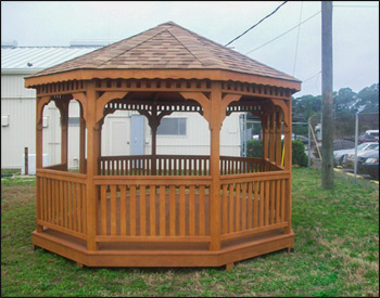 12 x 18 Treated Pine Oval Gazebo shown with Treated Pine Deck, 1x3 Railing, No Cupola, Rustic Cedar Asphalt Shingles, Cedar Stain, Hurricane Package, and Wavy Fascia. 