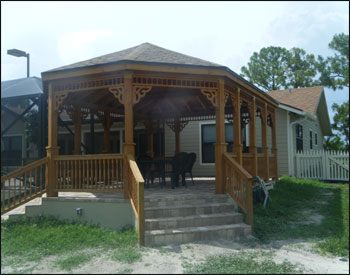 16x22 Treated Pine Custom Gazebo shown with One Rectangular Hip End and One Oval Hip End, No Floor, 2x2 Decorative Spindle Railings, Decorative Braces,  Taller Posts, 36” Post Trim, Rustic Cedar Asphalt Shingles, Two Coats Cedar Toned Stain and Sealer, and Hurricane Package