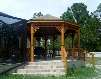 16x22 Treated Pine Custom Gazebo shown with One Rectangular Hip End and One Oval Hip End, No Floor, 2x2 Decorative Spindle Railings, Decorative Braces,  Taller Posts, 36” Post Trim, Rustic Cedar Asphalt Shingles, Two Coats Cedar Toned Stain and Sealer, and Hurricane Package