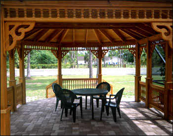 16x22 Treated Pine Custom Gazebo shown with One Rectangular Hip End and One Oval Hip End, No Floor, 2x2 Decorative Spindle Railings, Decorative Braces,  Taller Posts, 36” Post Trim, Rustic Cedar Asphalt Shingles, Two Coats Cedar Toned Stain and Sealer, and Hurricane Package