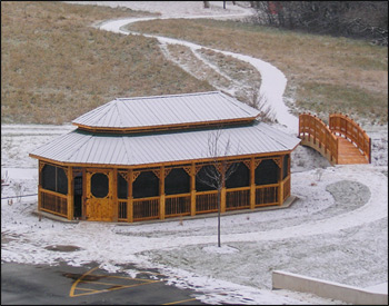 20’ x 36’ Cedar Double Roof Oval Gazebo shown Optional 2x2 Turned Spindle Railings, Decorative Braces, 4 Track Window System, Evergreen Metal Roof and Cedar Tone Stain Sealer.