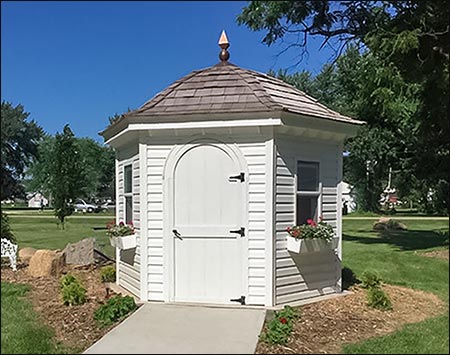 10' Vinyl Hexagon Belle Cabana Shown in White Vinyl with Cedar Shake Shingles, Two Flower Boxes, Custom Finial, Custom Height Arched Door, Custom Windows, and Taller Walls.